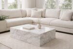 Modern neutral living room featuring a large stone coffee table with white marble veining, styled with a cream sectional sofa, soft cushions, and natural daylight.